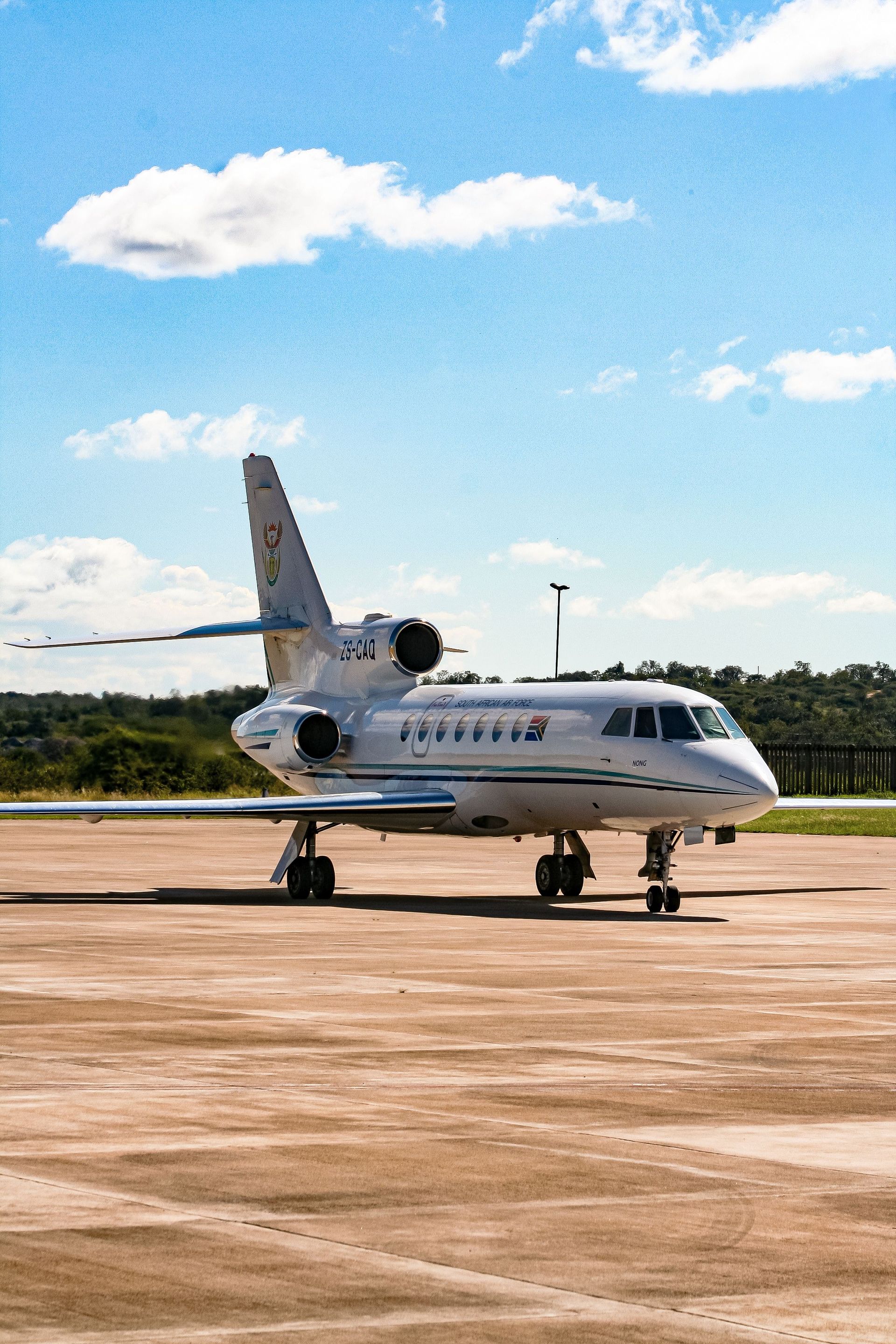 A sleek private jet sits on a sunlit runway against a blue sky in Eswatini.